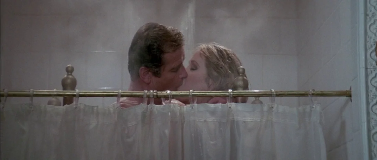 A View to a Kill (1985) movie still: medium — A tiled bathroom shower area is filled with thick, rising steam. A man and a woman stand behind a…
