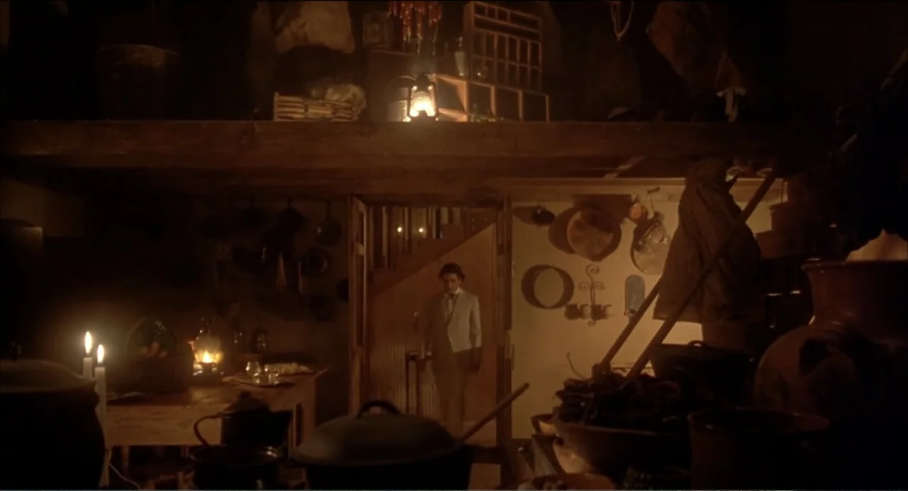 Like Water for Chocolate (1992) movie still: medium — A dimly lit rustic room filled with hanging kitchen utensils and dark wooden shelves. A man in…