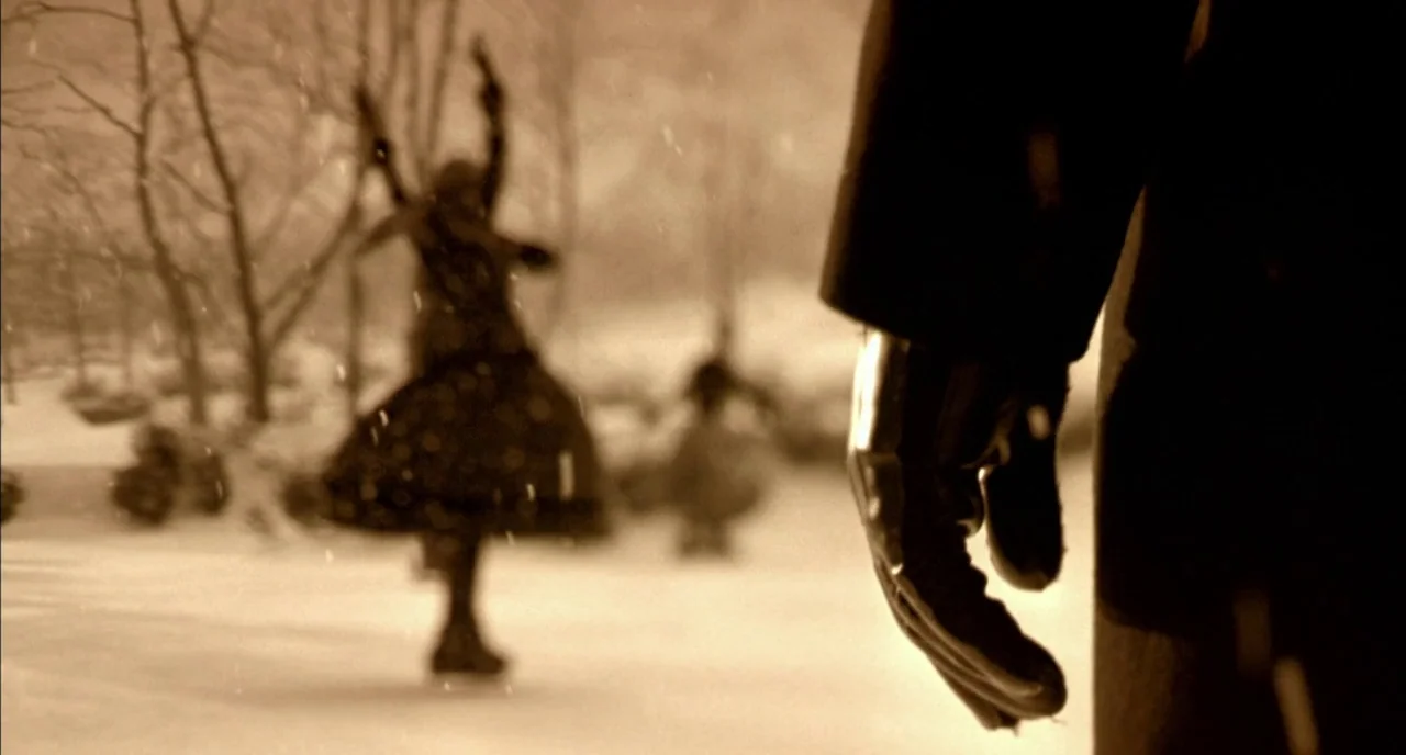 In The Cut (2003) movie still: closeup — A snowy outdoor ice rink features figures skating in the blurred background. A close-up shows a gloved hand…