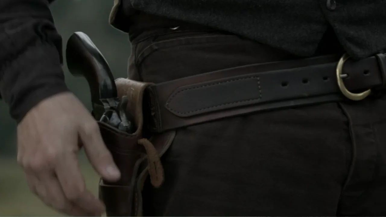 Dawn Rider (2012) movie still: closeup — A close-up shot focuses on a brown leather gun belt worn over dark trousers. A hand is positioned near the…