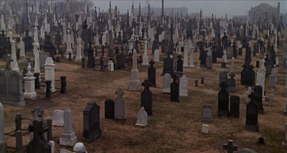 Midnight Cowboy (1969) movie still: wide — A dense urban cemetery features rows of weathered stone monuments and grave markers. The overcast…