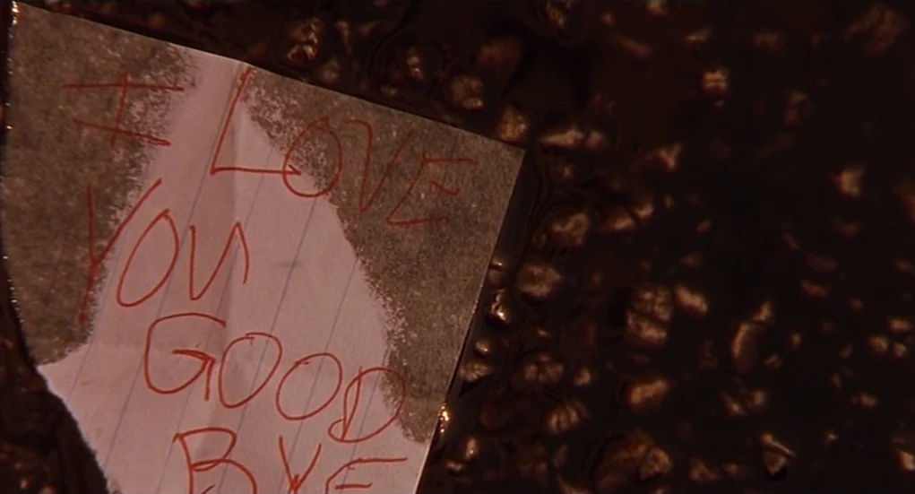 The Heart Is Deceitful Above All Things (2004) movie still: closeup — A torn piece of lined notebook paper rests in a dark, murky puddle. Red ink on…