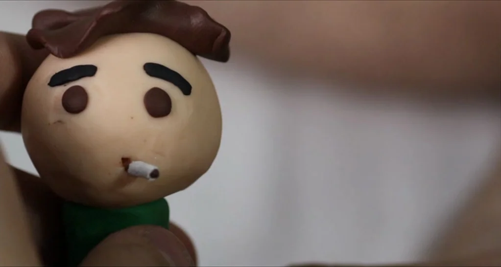 I Killed My Mother (J’ai tué ma mère) (2009) movie still: closeup — A miniature clay character head rests between two fingers against a blurred…