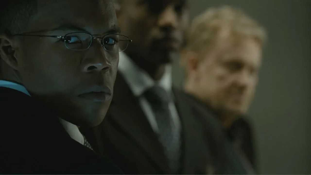 Salt (2010) movie still: closeup — A dimly lit corporate hallway features three men standing in a shallow depth line. The foreground man wearing…