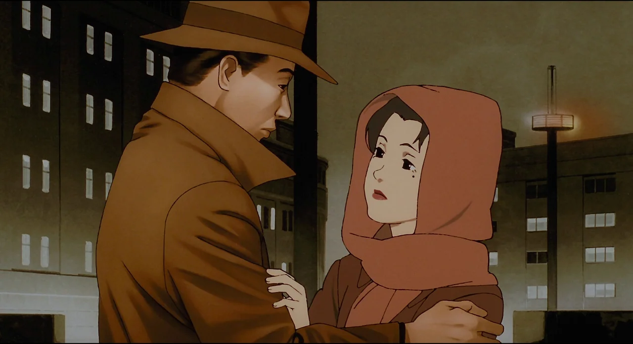 Millenium Actress (2001) movie still: medium — A man and woman embrace on a city street at night in front of buildings. The man wears a trench coat…