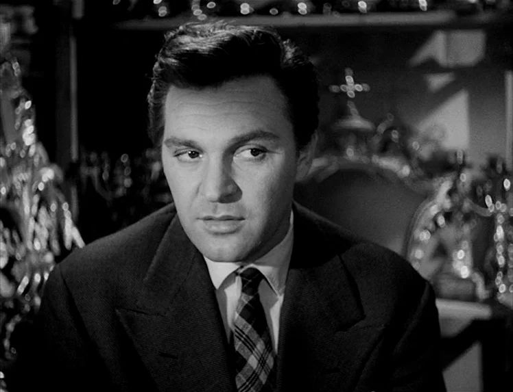 I Vitelloni (1953) movie still: closeup — An interior space filled with blurred reflective metallic ornaments and shop decor. A man in a suit looks…