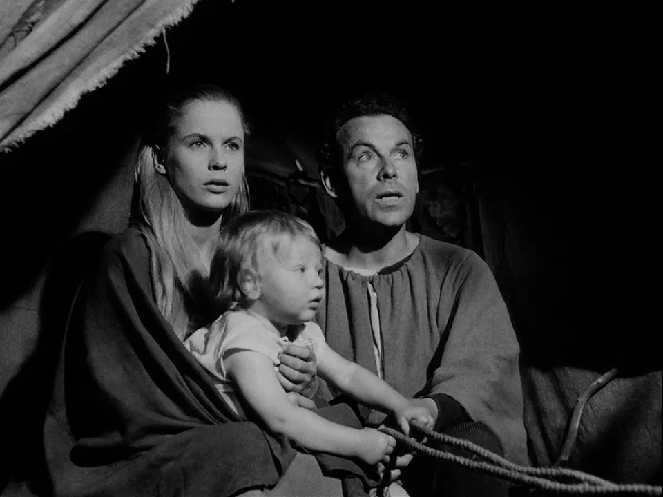 The Seventh Seal (1957) movie still: medium — A dark, cramped space with thick fabric folds in the corner. A man and woman sit holding a child while…