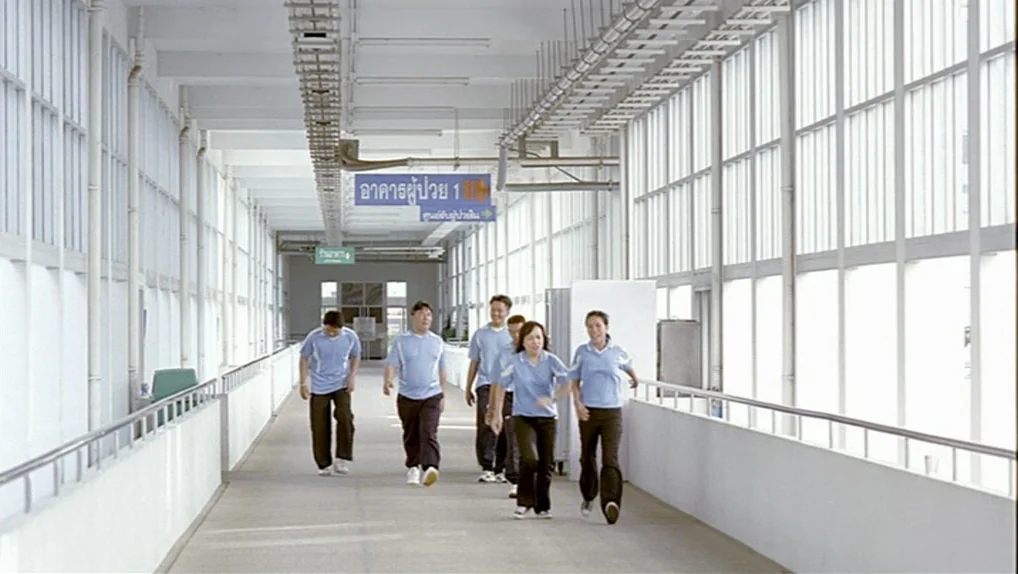 Syndromes and a Century (2006) movie still: wide — A long, bright hospital walkway with white walls and floor-to-ceiling windows on both sides. A…