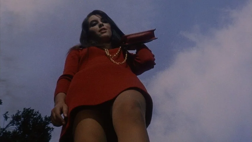 Four Times that Night (1971) movie still: fullbody — A woman stands under a bright blue sky filled with scattered white clouds. She gazes downward…