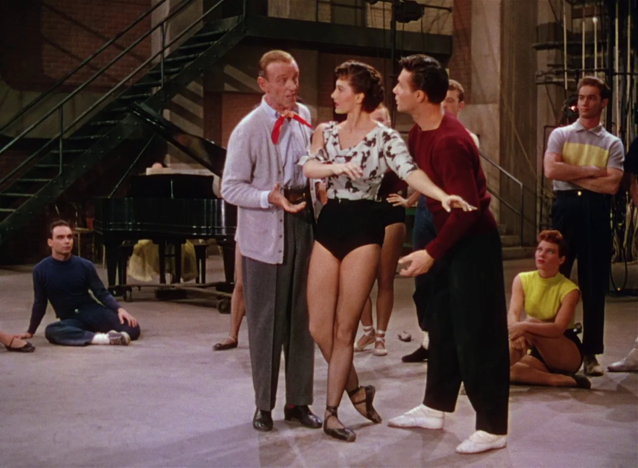 The Band Wagon (1953) movie still: fullbody — A spacious dance practice room features a metal staircase and a grand piano nearby. Several dancers…