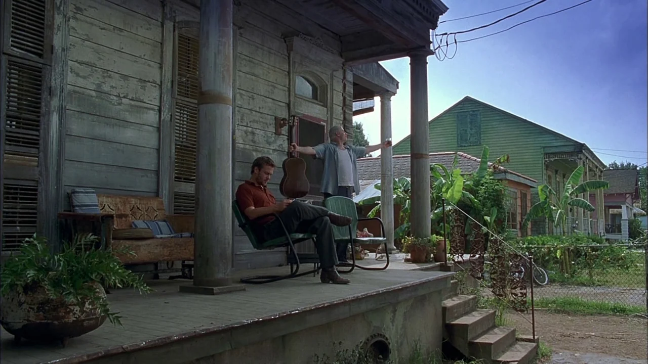 Love Song For Bobby Long (2004) movie still: wide — A weathered wooden house porch features flaking paint and tall classical columns. Two men occupy…