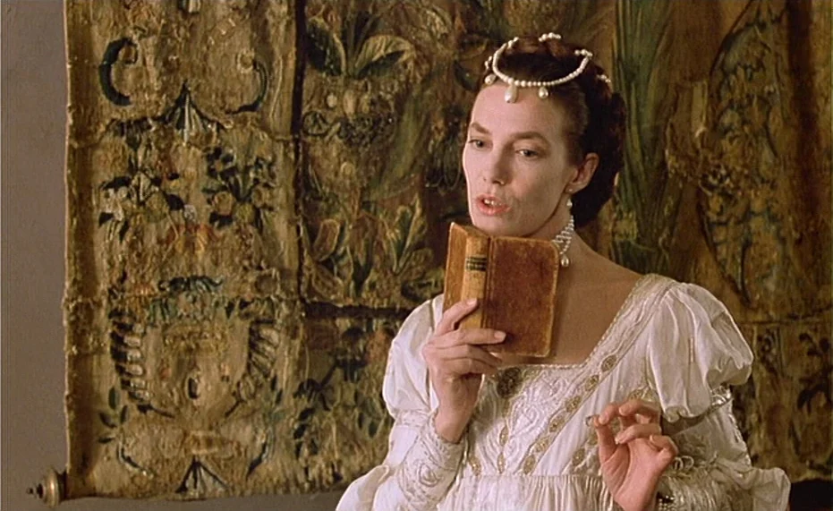Jane B. par Agnès V. (1988) movie still: medium — A historic interior features a textured, embroidered tapestry hanging behind a woman. The woman…