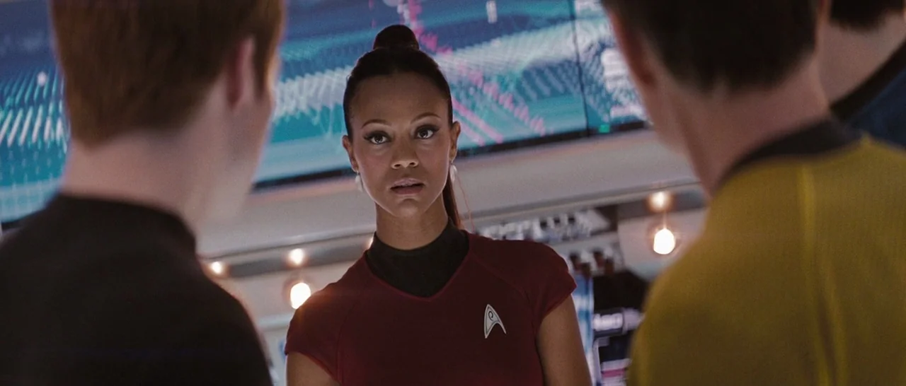 Star Trek (2009) movie still: medium — A futuristic command center displays data on large glowing blue panels behind the subject. A woman in a red…