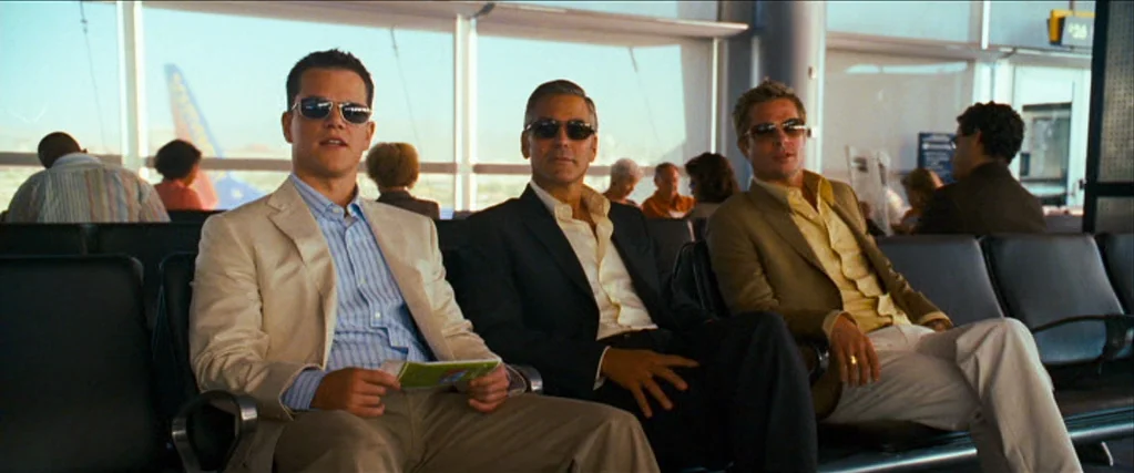 Ocean’s Thirteen (2007) movie still: medium — An airport boarding lounge features floor-to-ceiling windows overlooking a plane on the tarmac. Three…