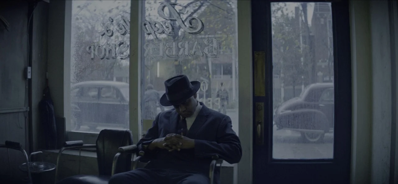 No Sudden Move (2021) movie still: medium — A 1950s shop interior with a storefront window featuring painted lettering. A man sits in a vintage…