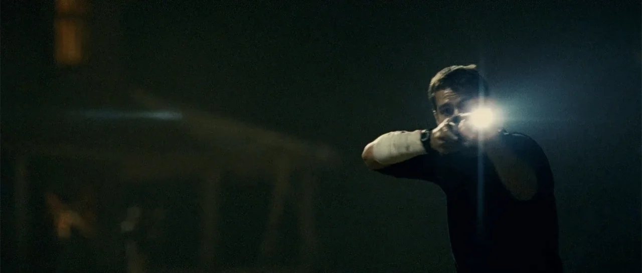 Blood Creek (2009) movie still: medium — A man stands in a dark exterior environment during the night. He aims a tactical flashlight and firearm…
