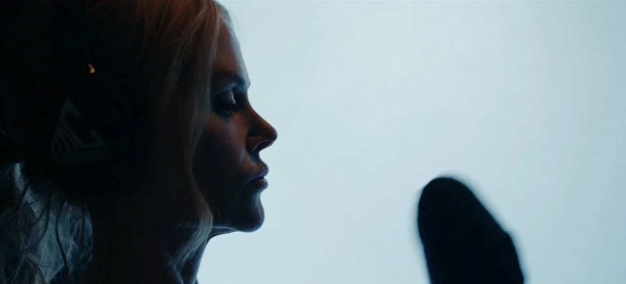 Babygirl (2024) movie still: closeup — A woman stands in a brightly backlit recording studio space with an out-of-focus microphone. She wears large…