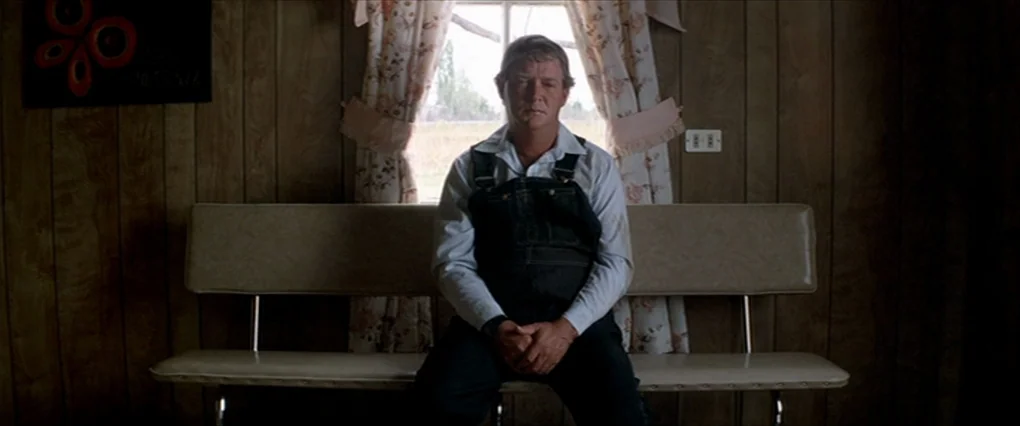 Silent Light (2007) movie still: medium — A room with paneled walls and a vinyl bench positioned before a window with curtains. A middle-aged man in…
