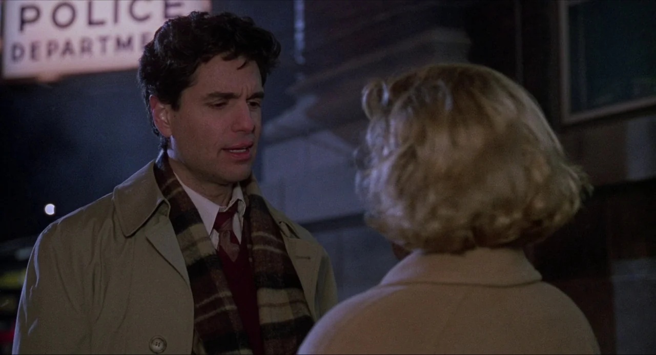 Child’s Play (1988) movie still: medium — A man and woman stand outside a building at night. A brightly lit sign reads Police Department on the dark…
