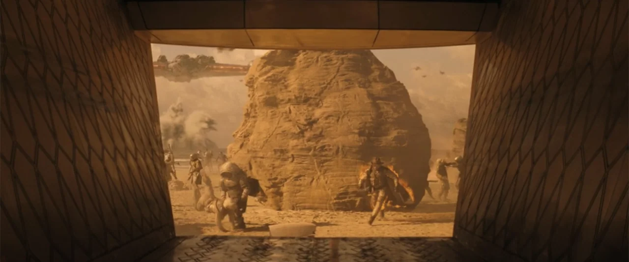 The Fall Guy (2024) movie still: wide — A futuristic beach landscape features a large, weathered rock formation on the golden sand. Various armored…