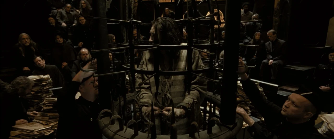 Harry Potter and the Goblet of Fire (2005) movie still: medium — A dark subterranean hall features rows of seated observers watching a central iron…