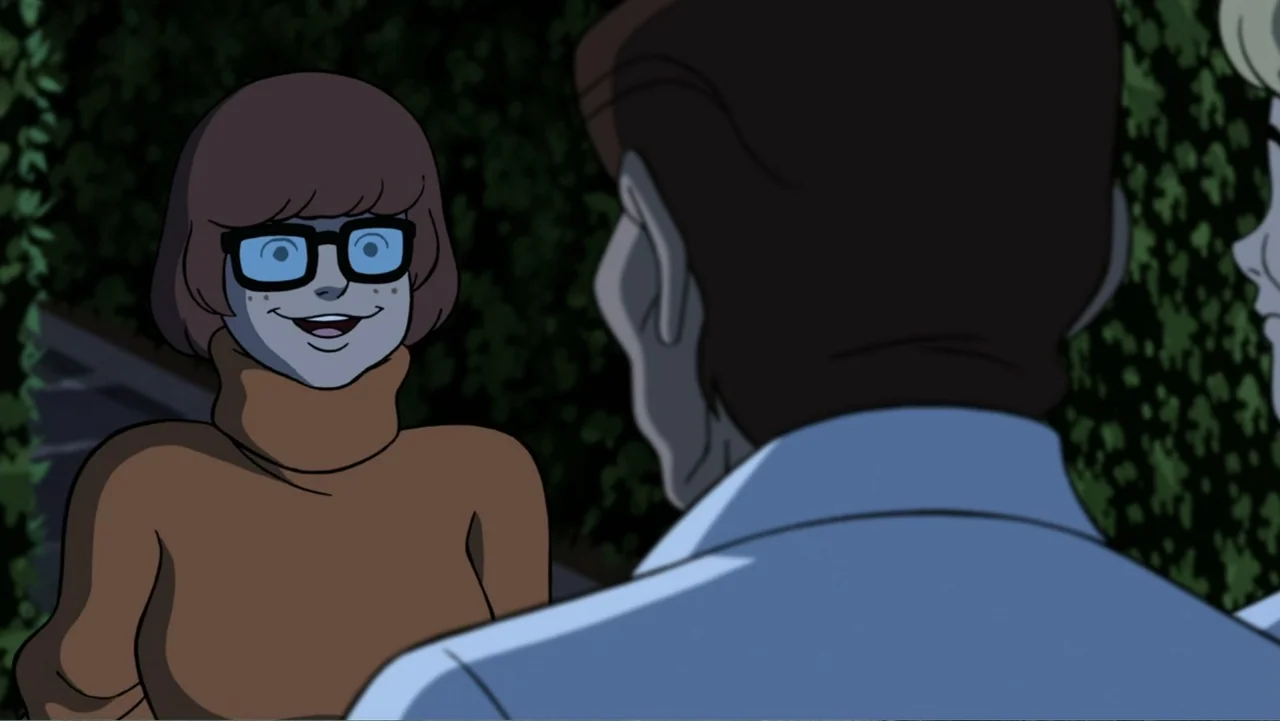 Scooby-Doo! and the Gourmet Ghost (2018) movie still: medium — A dark outdoor space with dense green foliage in the background. A woman in a brown…