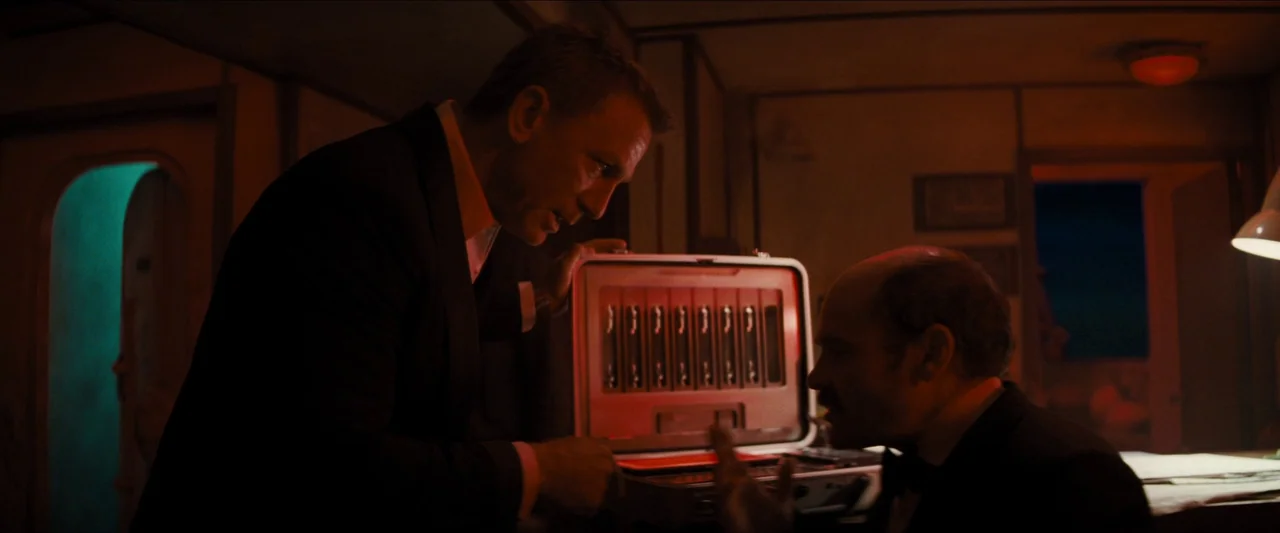 No Time To Die (2021) movie still: medium — A cramped train compartment features wood-paneled walls and a dim, warm-toned interior atmosphere. A man…