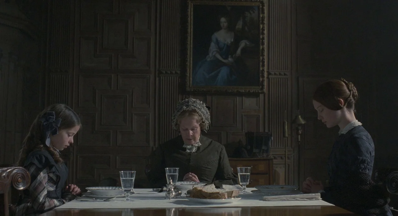 Jane Eyre (2011) movie still: medium — A dark dining room with wood-paneled walls and a large oil painting. Three women sit at a dining table with…