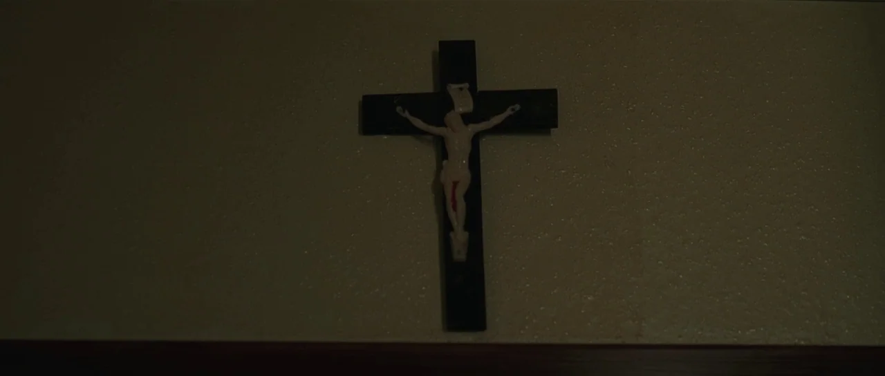 Bullhead (2011) movie still: closeup — A dark, textured plaster wall serves as the backdrop for a small wall-mounted object. A black crucifix with a…