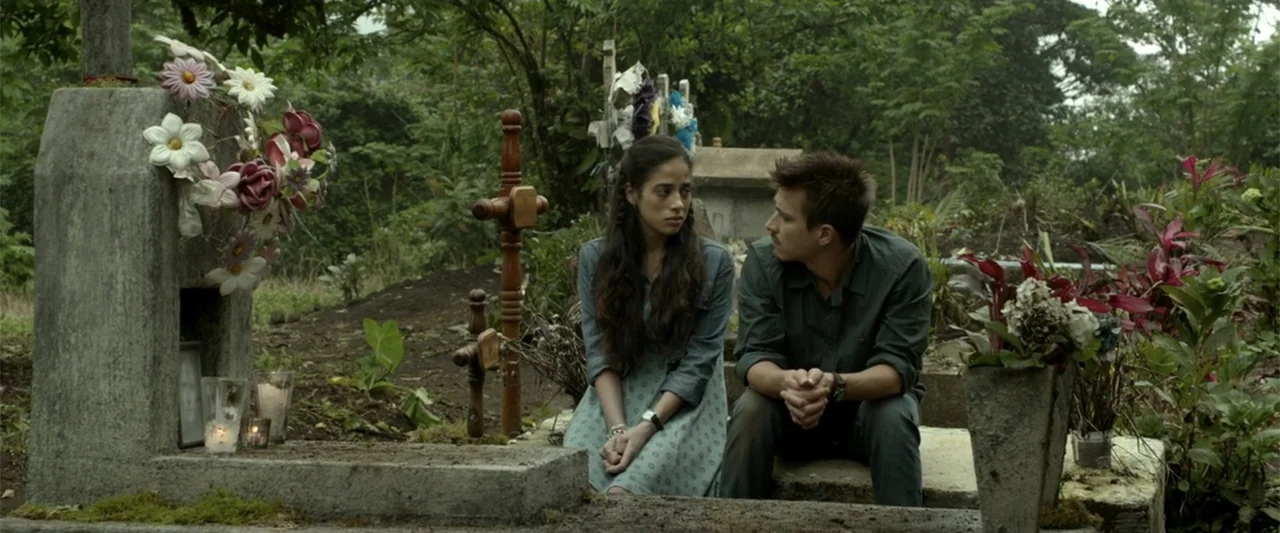 I Dream in Another Language (2017) movie still: medium — A quiet cemetery filled with lush green foliage and weathered stone monuments. A young man…