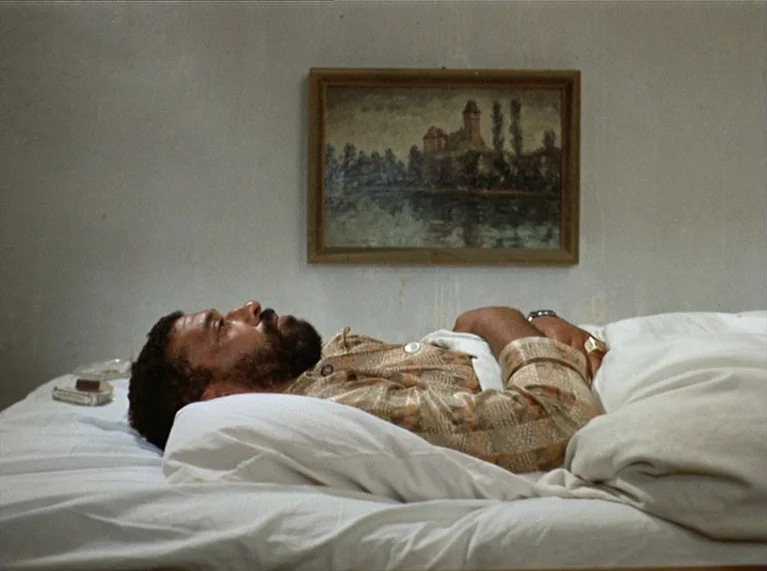 Ali: Fear Eats The Soul (1974) movie still: medium — A plain white-walled space with a landscape painting hung above a simple bed frame. A man with…