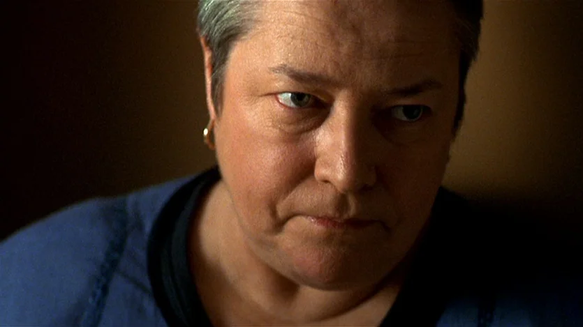 Love Liza (2002) movie still: closeup — A close-up shot of an older woman's face against a dark, featureless background. The woman looks slightly…