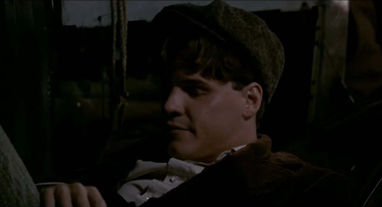 A River Runs Through It (1992) movie still: closeup — The interior of a dimly lit, dark passenger transport cabin at night. A young man in a tweed…