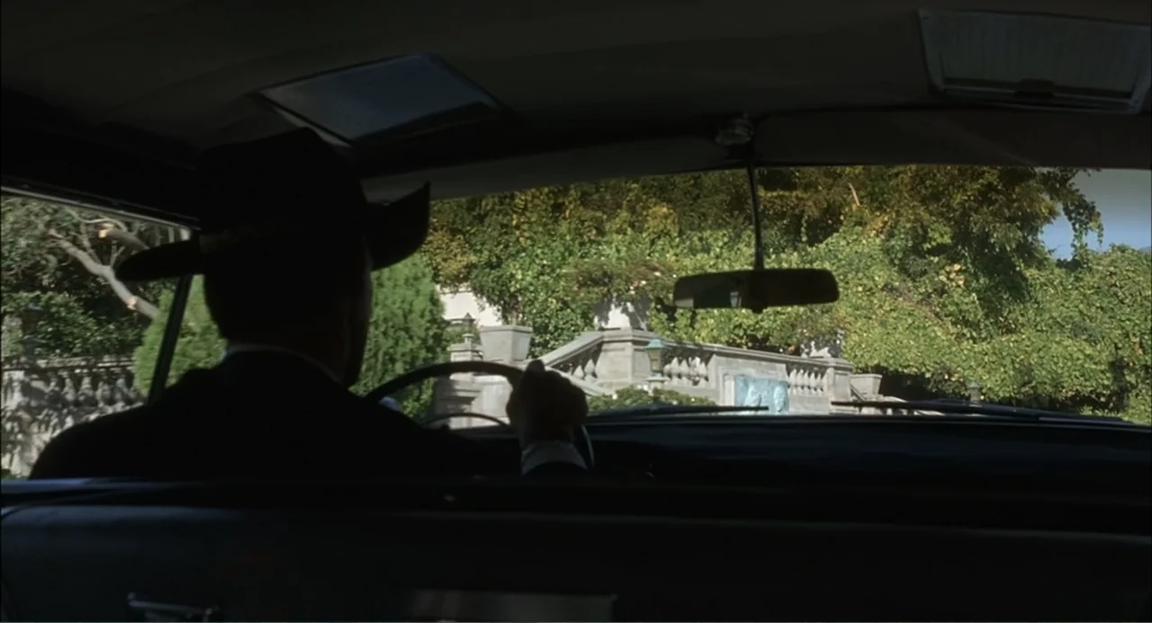 Wild Orchid II: Two Shades of Blue (1991) movie still: medium — A view from inside a car looking out over the dashboard at a garden. A man in a suit…