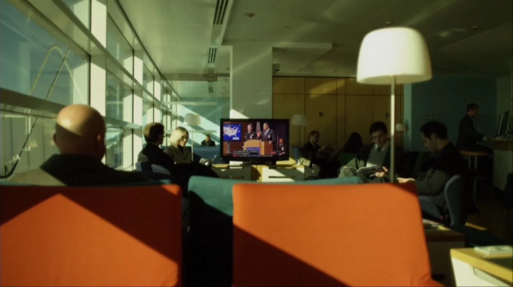 Contagion (2011) movie still: wide — An airport waiting lounge features rows of bright orange chairs near tall glass windows. Multiple travelers sit…
