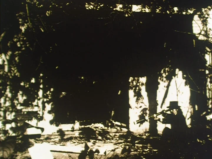 The Reading Machine (1977) movie still: wide — A dilapidated structure overgrown with vines is illuminated by bright daylight through gaps. A lone…