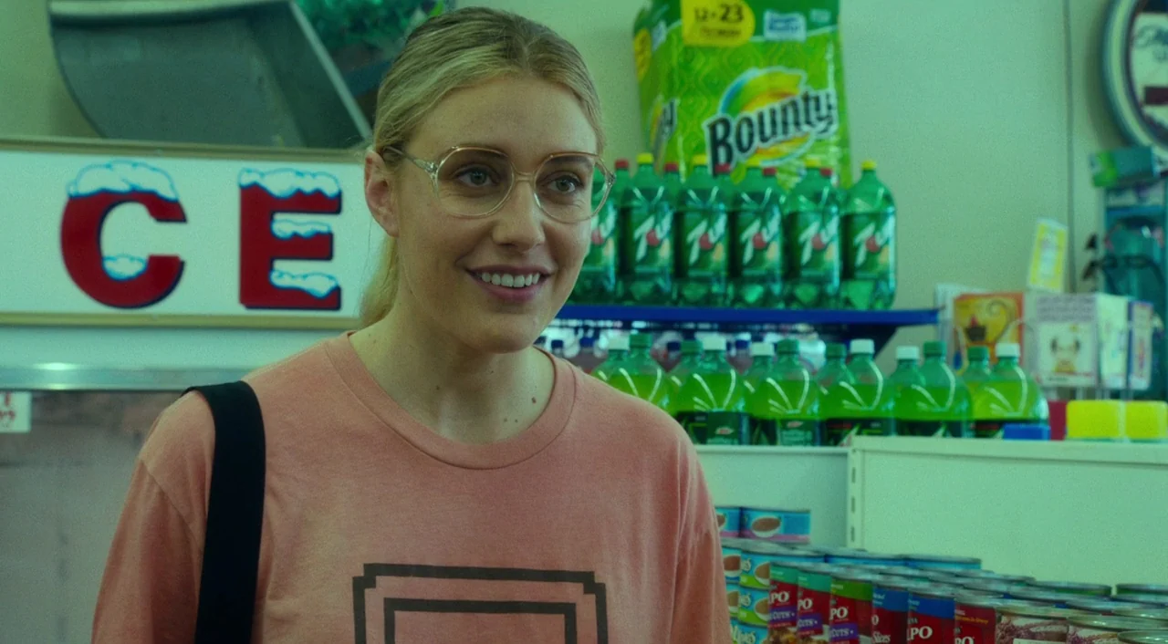 Wiener-Dog (2016) movie still: medium — A well-stocked convenience store aisle features stacked cans and rows of green soda bottles. A woman in a…