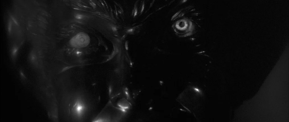 The Innocents (1961) movie still: closeup — A man's face emerges from total darkness in a high-contrast close-up shot. His eyes are illuminated by a…
