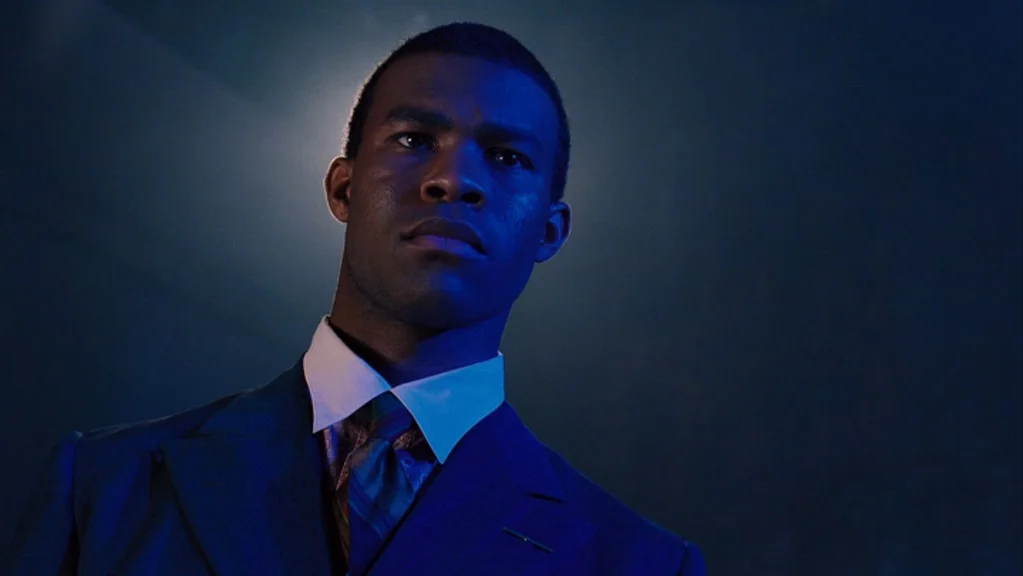 Honeydripper (2007) movie still: medium — A man in a formal suit stands against a dark, minimalist wall in shadow. He faces forward while…