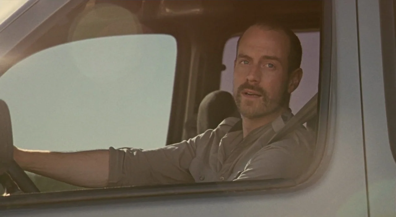 Patagonia (2010) movie still: medium — A man sits in the driver seat of a vehicle during the day. He holds the steering wheel while looking ahead…