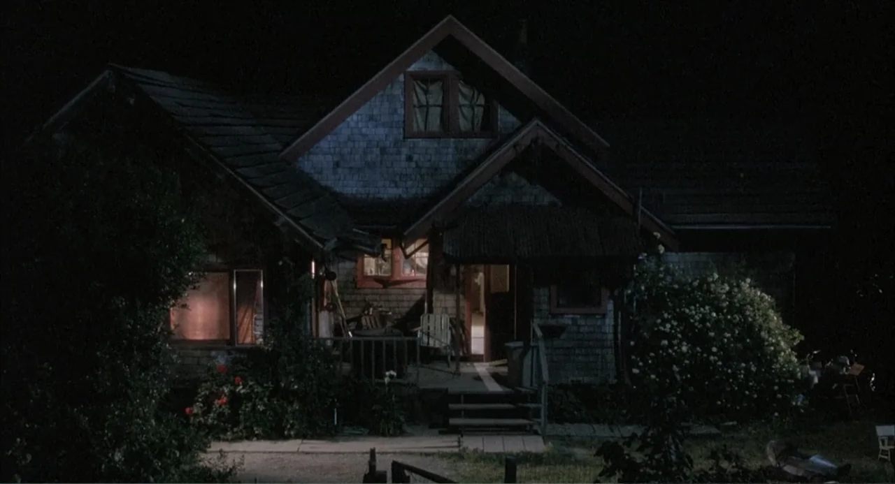 Overboard (1987) movie still: establishing — A two-story shingle-sided house stands in darkness at night. The front door and several windows are…