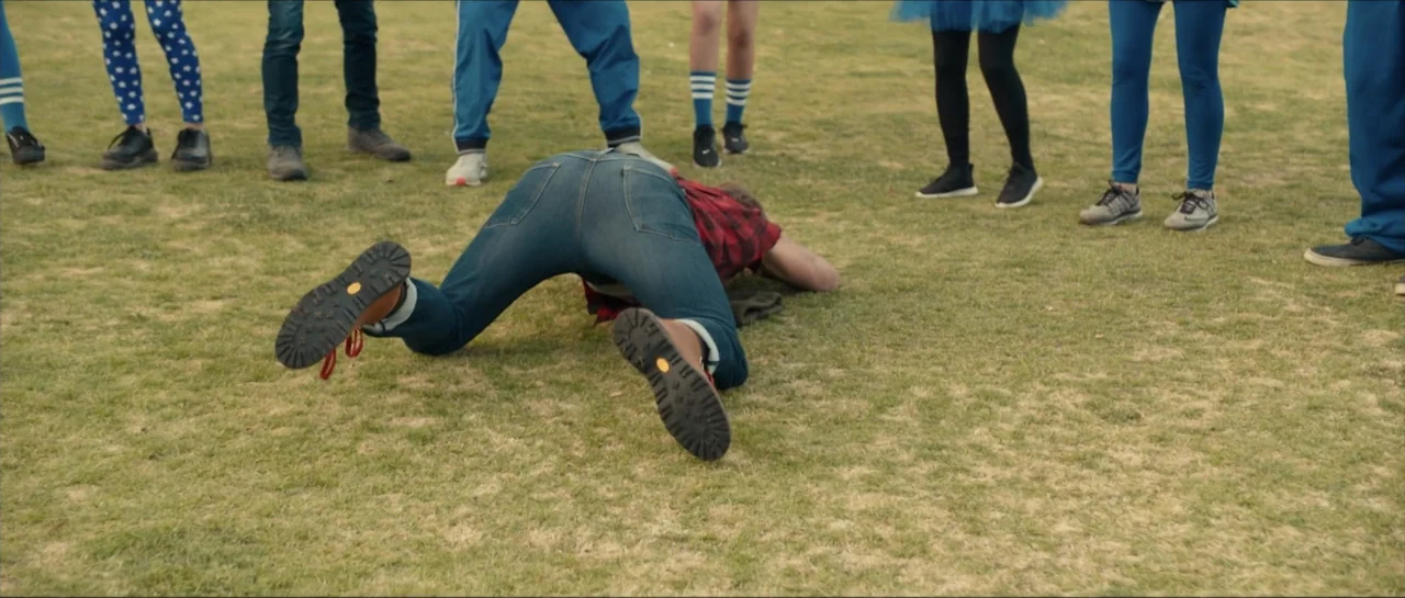 We Broke Up (2021) movie still: fullbody — A group of people wearing casual athletic clothing stand on a large grass field. One individual is on…