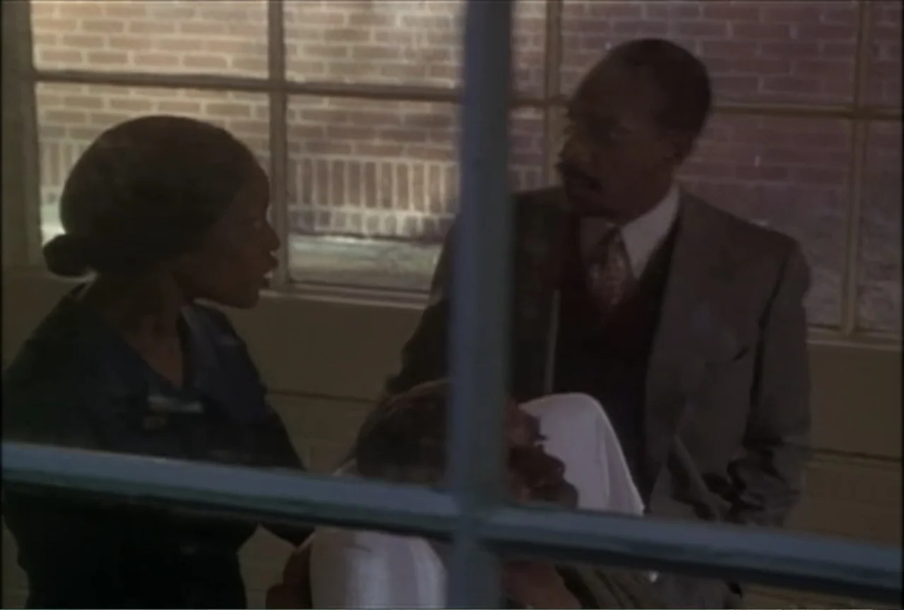 Miss Evers' Boys (1997) movie still: medium — A hospital room with a large window and exposed brick wall background. A woman in dark clothing and a…