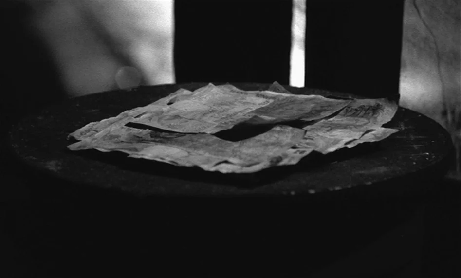 The Man From London (2007) movie still: closeup — A pile of rumpled paper currency sits on a dark, circular wooden surface. The background is…
