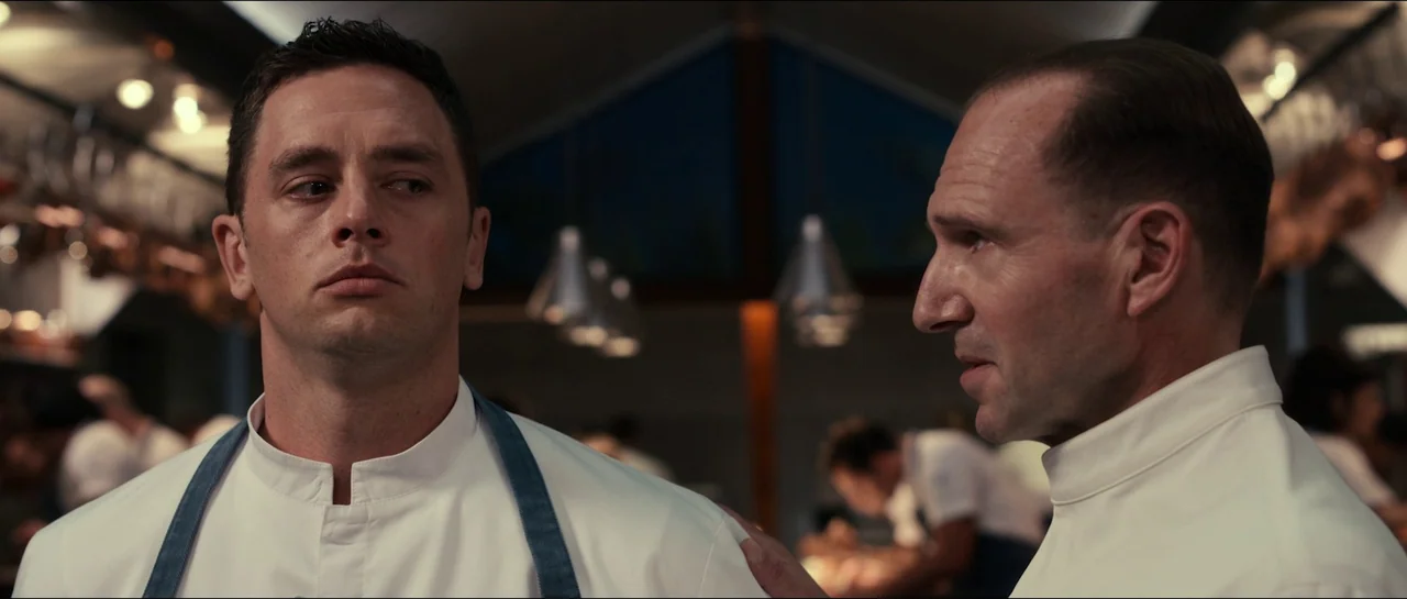 The Menu (2022) movie still: medium — A sterile, modern industrial professional cooking space with high ceilings and metallic decor. One chef…