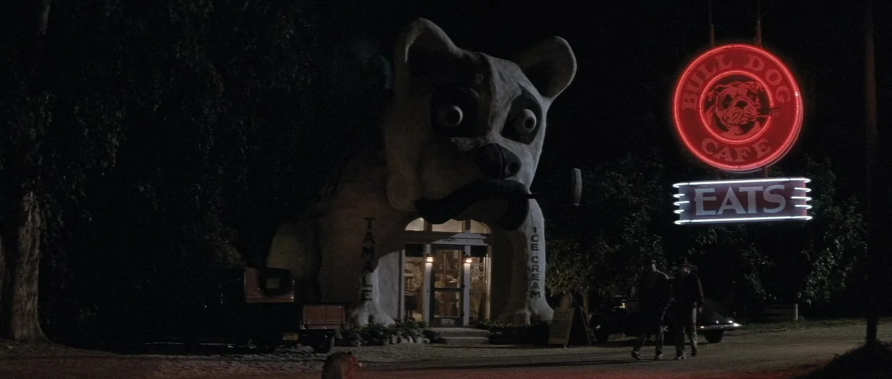 The Rocketeer (1991) movie still: wide — A giant dog-shaped novelty building sits beside a dirt road under a night sky. A glowing neon sign hangs…