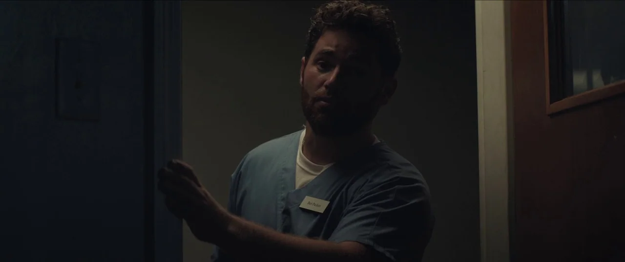 The Peanut Butter Falcon (2019) movie still: medium — A dark, shadowed corridor with a doorway frame visible on the left and right. A man in blue…