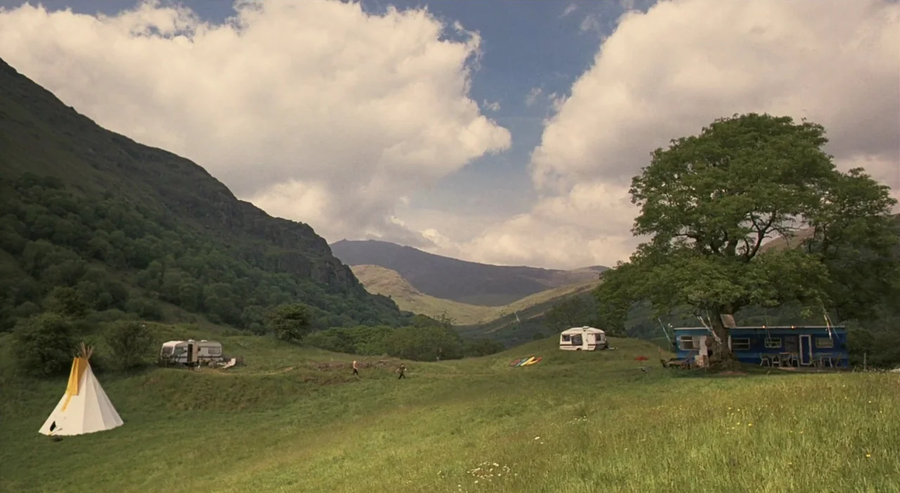 Patagonia (2010) movie still: establishing — A wide valley landscape features grassy hills dotted with several mobile caravans and a teepee. Two…