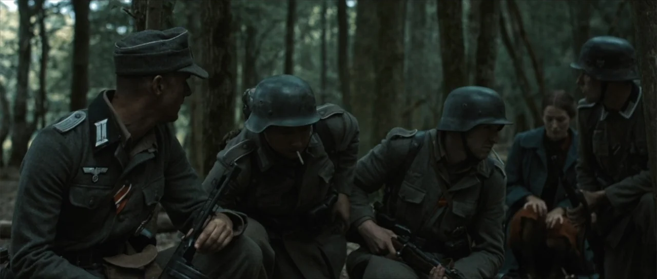 Sin retorno (2009) movie still: medium — A dense group of soldiers and a woman gather in a thick forest environment. The armed men in uniforms…