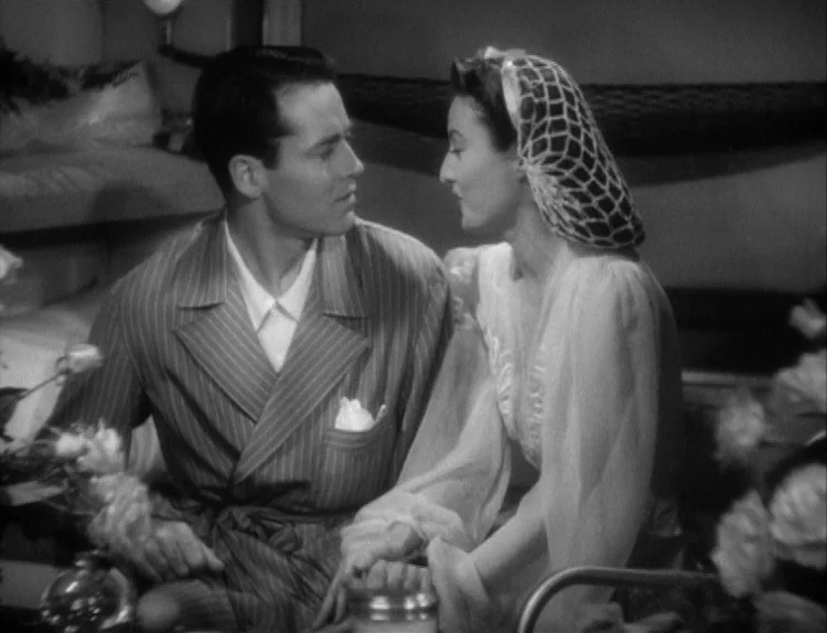 The Lady Eve (1941) movie still: medium — A bedroom set with soft bedding and flowers in the foreground. A man and a woman in sleepwear sit together…